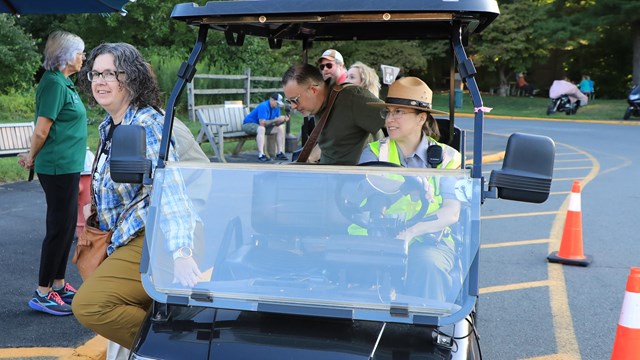 A ranger drops off patrons in a six passenger golf cart. 