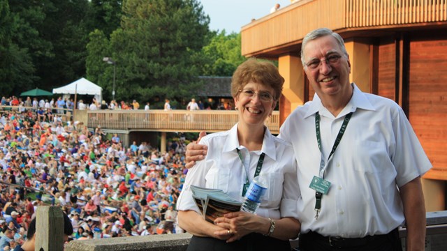 Two ushers pose with the Filene Center and patron in the background