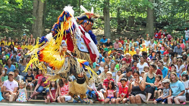 Native American in traditional dress dancing in front of an audience.
