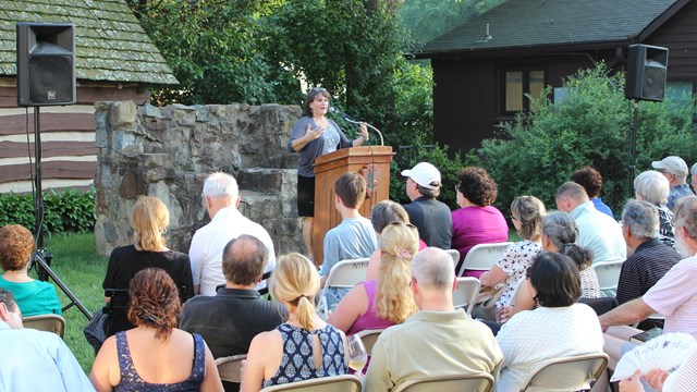 Speaker discussing the performance to patrons seated on Farmhouse Lawn.