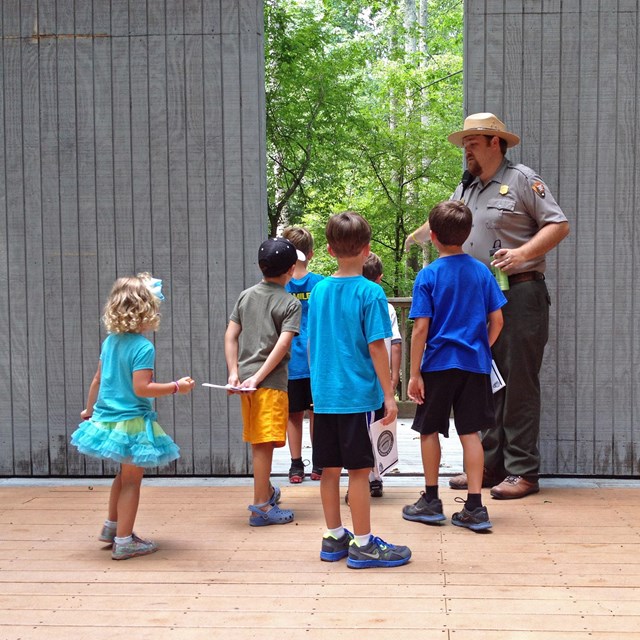 A ranger leads a program on stage with a group of children