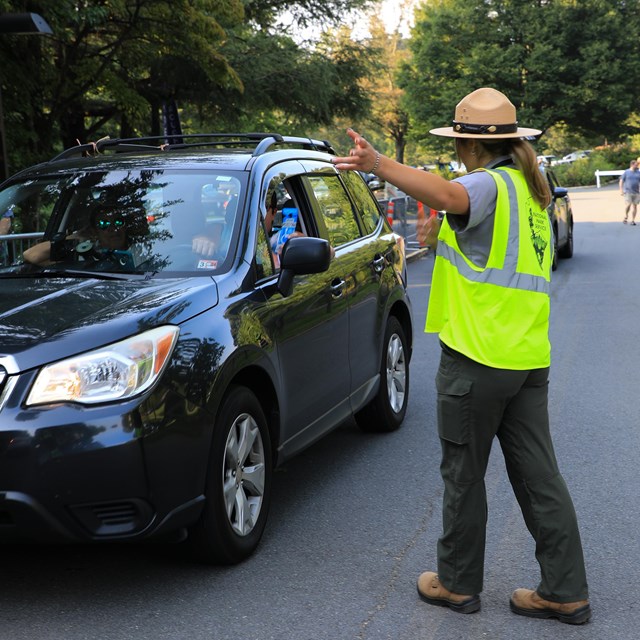 Female ranger giving directions to a car.