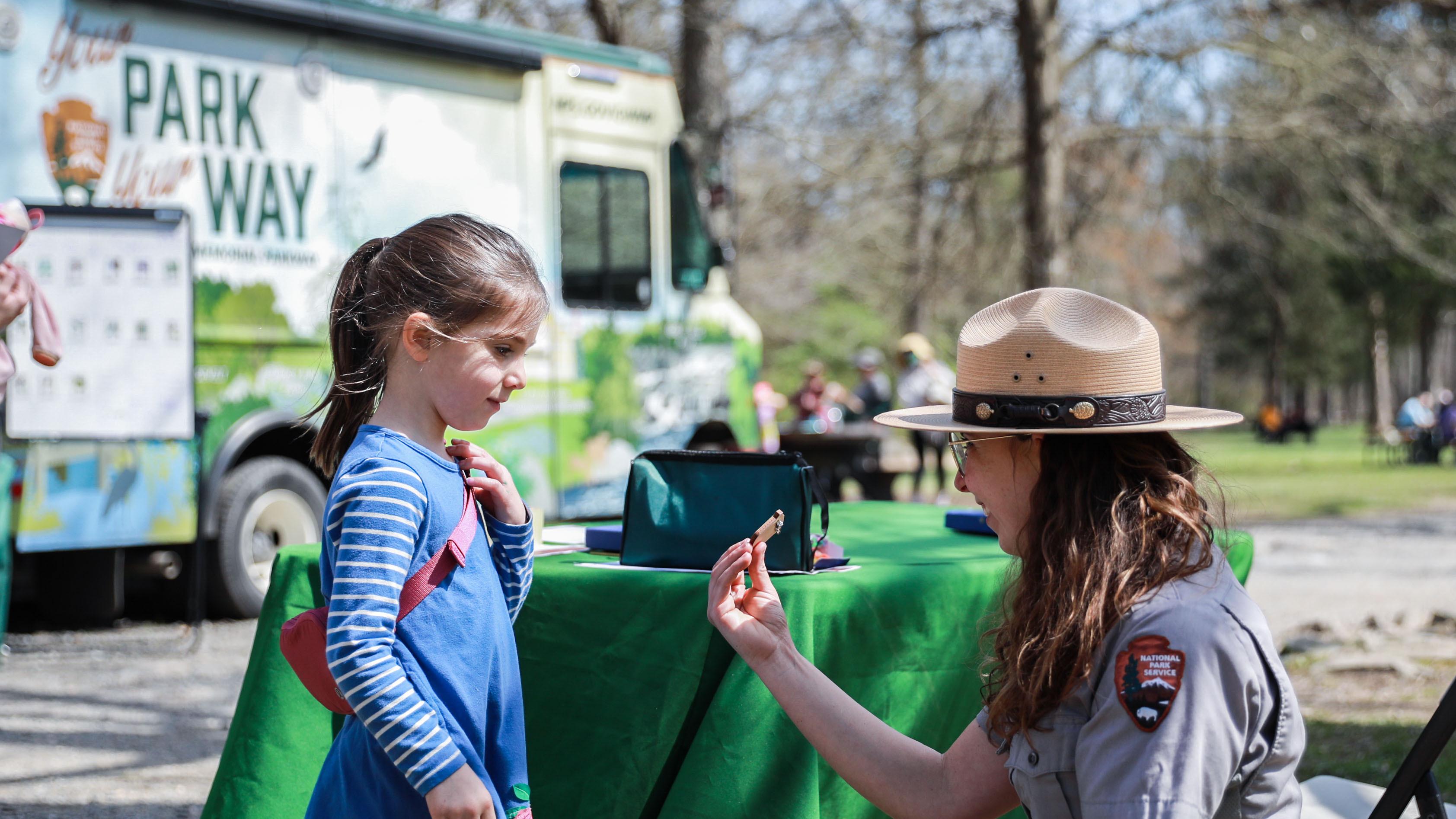 A ranger kneels down to give a junior ranger a badge