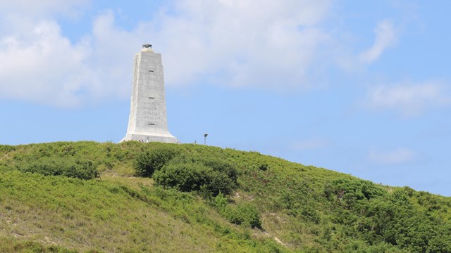 A large granite obelisk-like monument 60 feet tall on a grassy hill