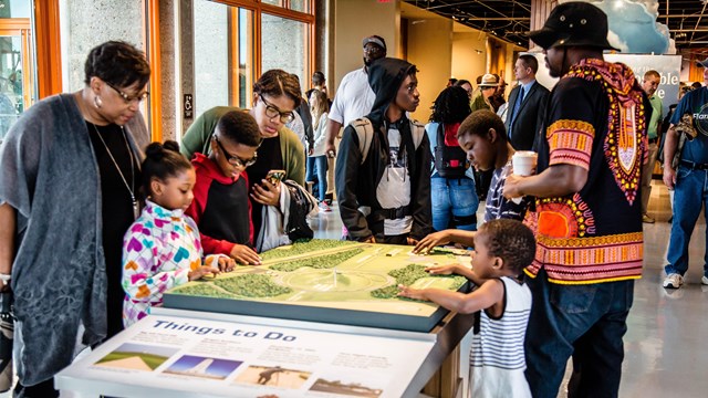 A group of people standing around a tactile map of Wright Brothers National Memorial