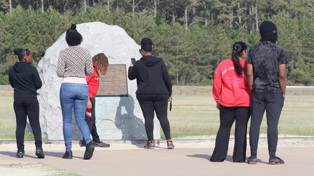 A group of adults and children near a large boulder with a plaque on it