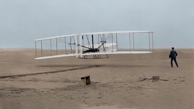Early bi-wing airplane taking off in a field of sand 