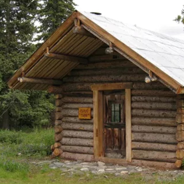 A wooden cabin sitting in a small clearing near a forest of trees and brush.