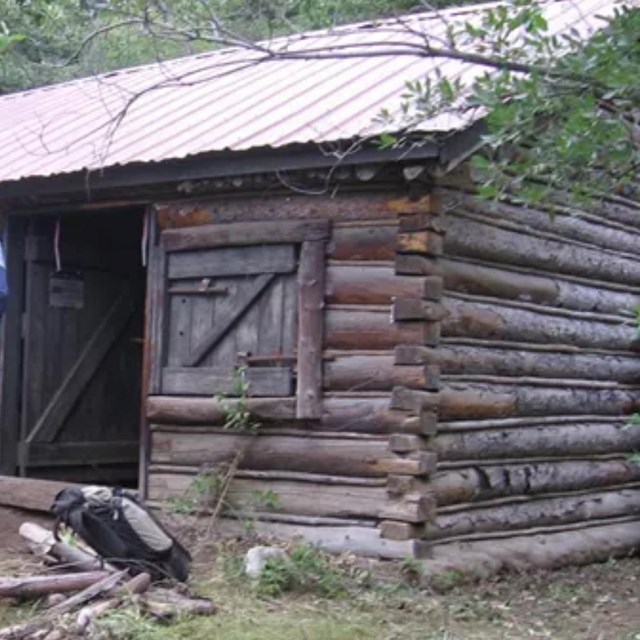 Three people inspecting a dark wood cabin.