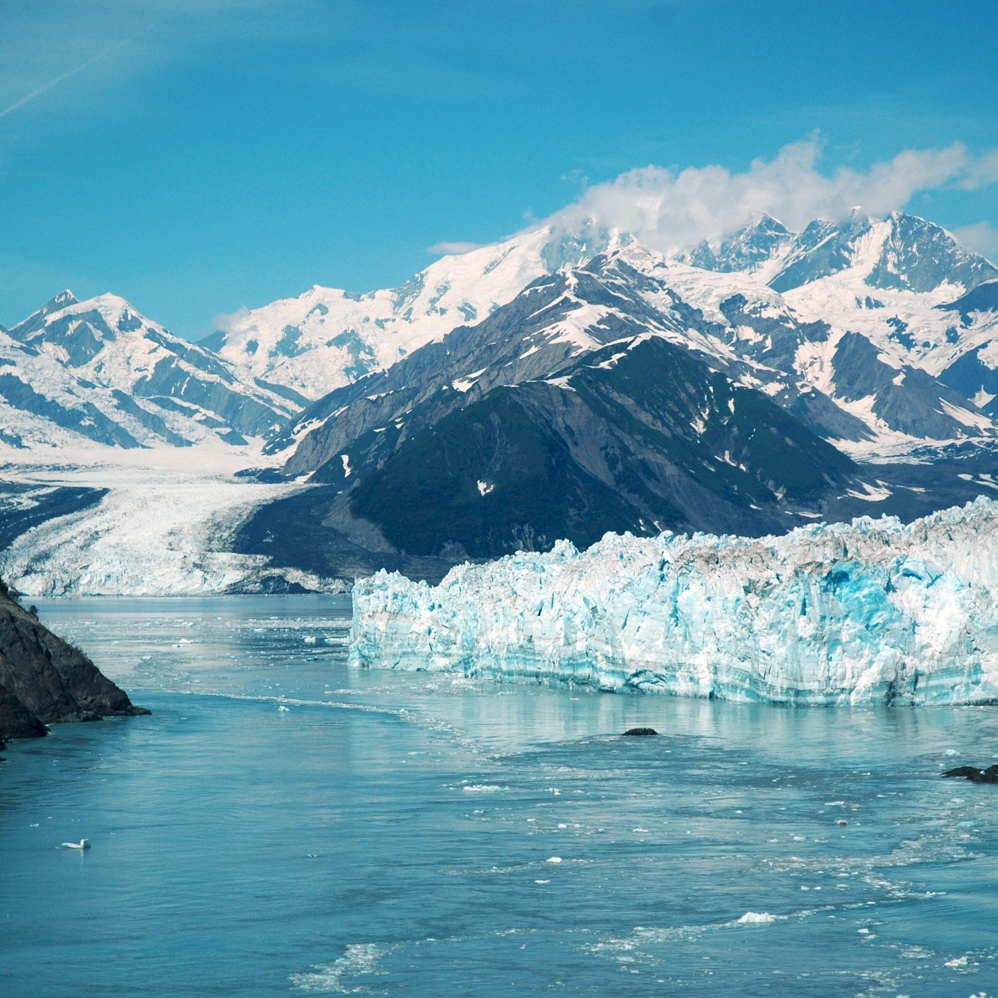 Hubbard Glacier flowing into the Gulf of Alaska with mountains and blue sky in the background.