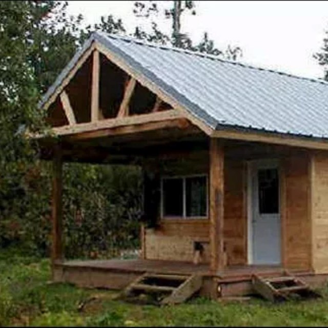 A tan wood cabin sitting in a forest clearing.