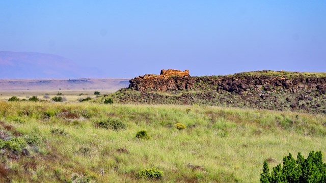 A desert landscape leads to a pueblo atop a rock outcropping, 