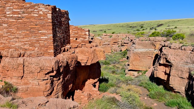 A sandstone pueblo next to a small canyon against a clear blue sky