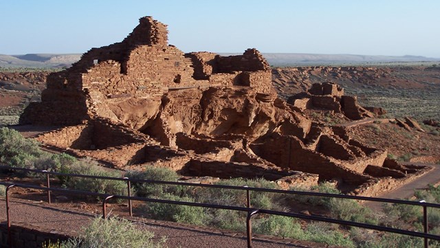 A partial three story sandstone structure with a surrounding trail and wide open landscape. 