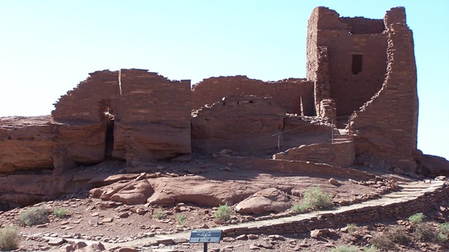 A three story rectangular tower structure made out of sandstone on top of a large rock outcrop. 