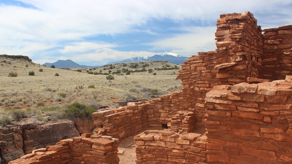 A partial two story stone structure with snow capped mountains in the background. 