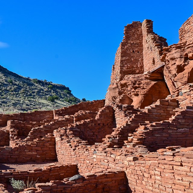 A red sandstone puebloan ruin with a mountain and blue sky in the background.