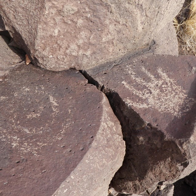 Large black basalt rocks with petroglyphs of a spiral and a human hand.