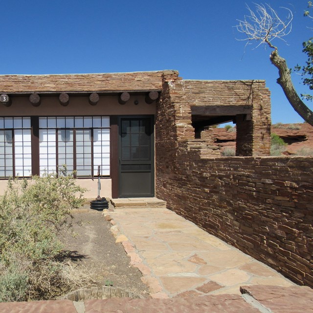 A stone house in the Pueblo Revival style with a small courtyard and three large front windows. 
