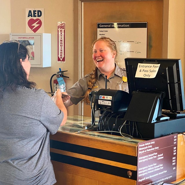 A smiling National Park Ranger speaks with a visitor in front of the visitor center kiosk.