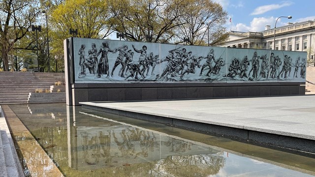 A pool of water in the foreground with a banner of life size depictions of soldiers in the bacground