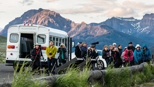 A group of people stand near a small tour bus.