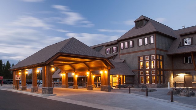 A large brown lodge is light under an evening sky.