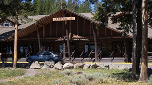 A car is parked in front of a low-profile, long wooden lodge.