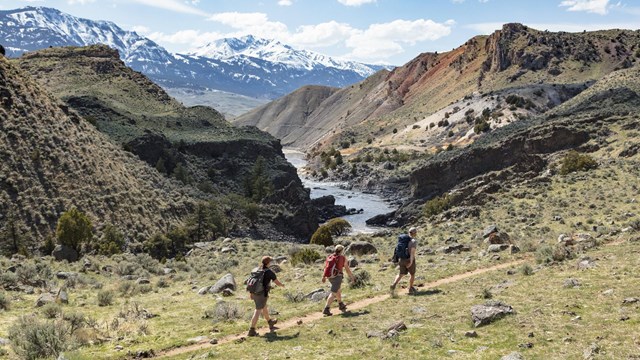 Hikers walking along a trail with river and mountain views.
