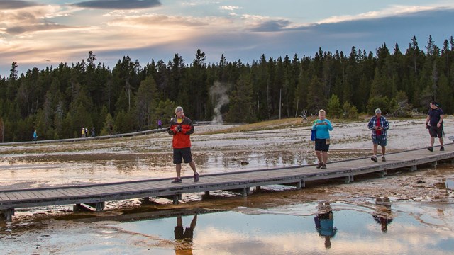 A group of people crossing a thermal area on a boardwalk.