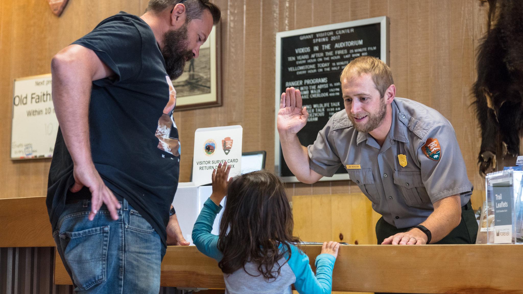 A park ranger holds up his right hand to swear in a young junior ranger while a man looks on.