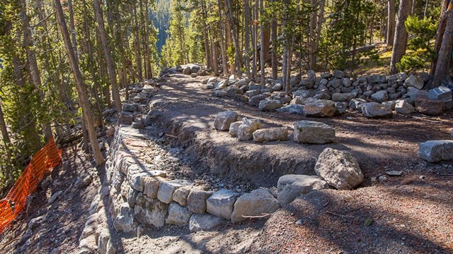 Trail with construction orange fencing around while rocks are moved into position.