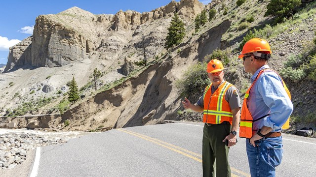 Two people in high-vis gear chatting near a road washout.
