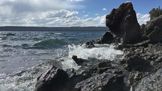 Volcanic rocks along the shore, with water crashing against them.