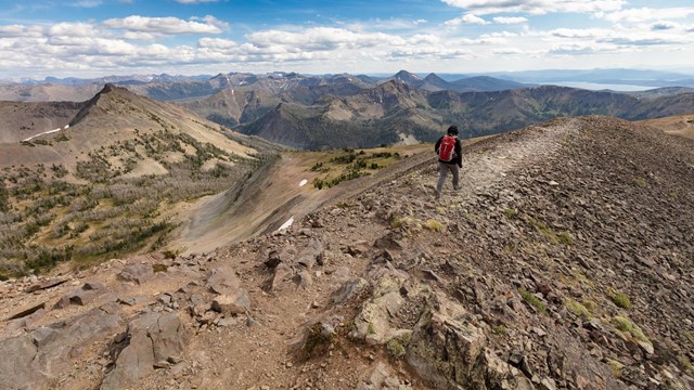 Hiker on a mountain ridge with a lake in the distance.