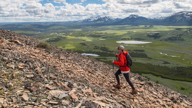 A person hikes up a trail with mountain views.