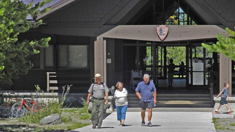 Two visitors walk with a ranger down a concrete path in front of the building.