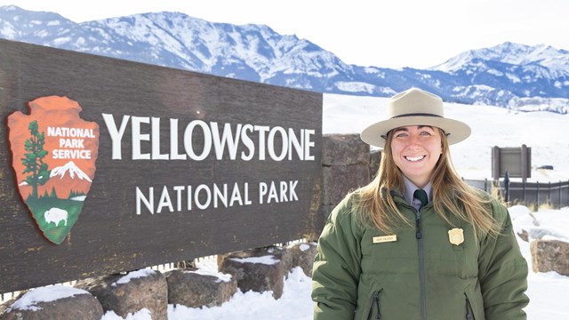 a park ranger in uniform smiling in front of a park sign