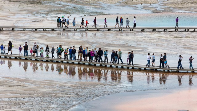 Visitors walk by hot springs along wooden boardwalks.
