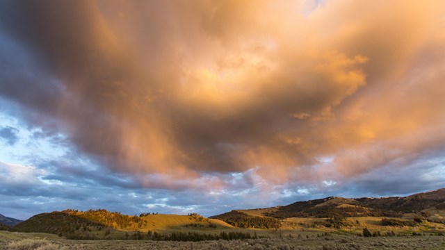 Sunlight colors overhead clouds with yellows, golds, and pinks.