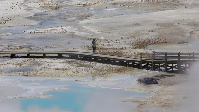 A person photographing the colors of hot springs from a boardwalk.