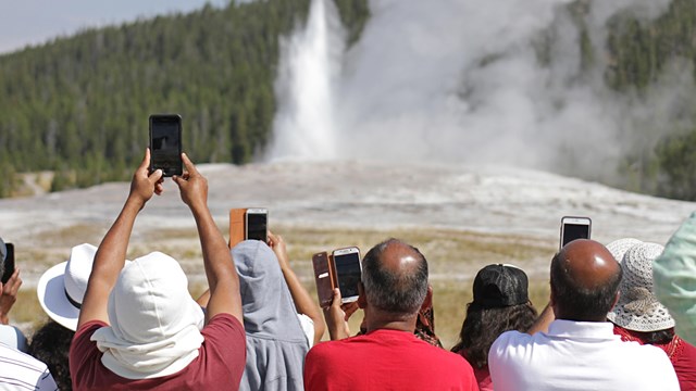 Visitors hold up their cellphones to take pictures of an erupting geyser.