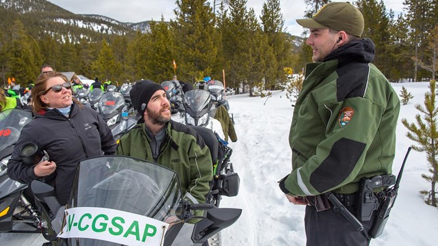Visitors on a snowmobile talk with a park ranger