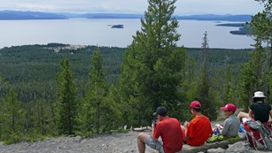 Hikers rest and look out at Yellowstone Lake from atop a mountaintop.