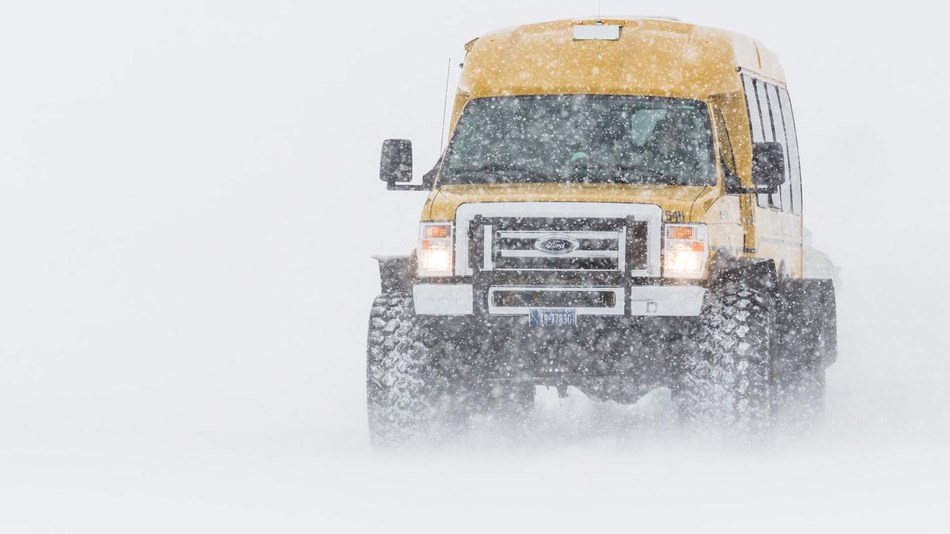 A large van travels over the snow in a blizzard