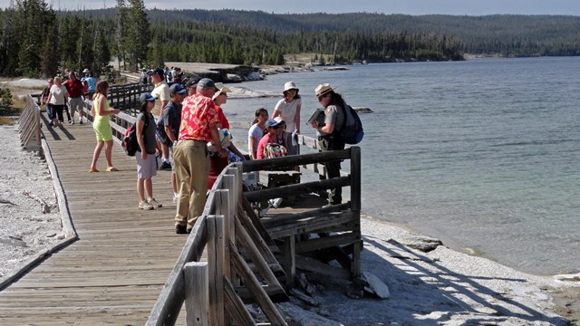 A park ranger stands on a boardwalk along a lakeshore and talks with visitors.