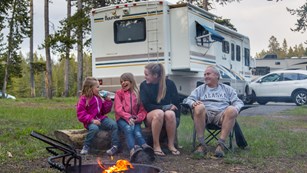 Four people sitting in campsite in front of a fire laughing and smiling.