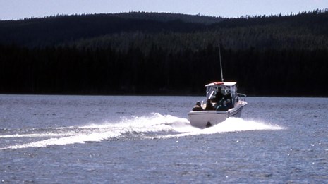 A motorboat crosses a large lake, creating a wake behind it.