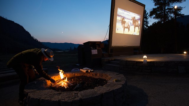 Park ranger starts a campfire at the start of a campground evening program.