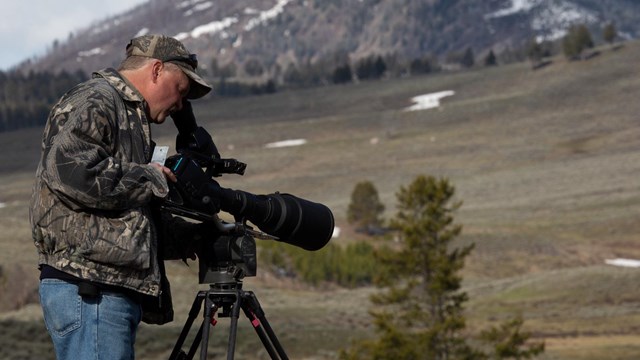 A videographer looks through his viewfinder of the video camera to frame a scene.